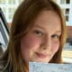 Smiling young woman in a car holding a Practical Driving Test pass certificate.