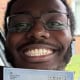 Smiling man wearing glasses holds up a Practical Driving Test Pass Certificate in front of a car window.